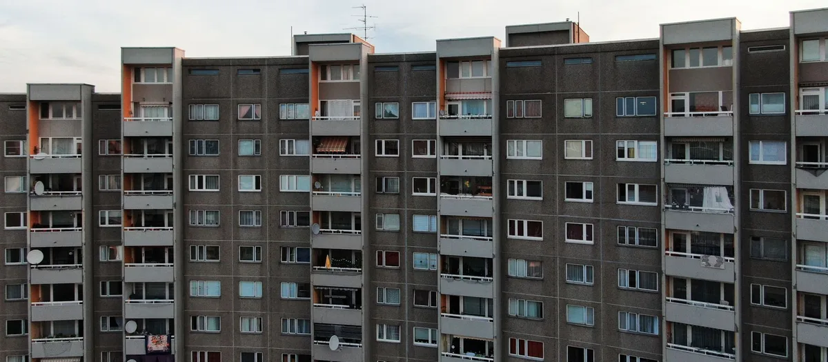 Lange Zeile eines Wohnblocks in Plattenbauweise mit Balkonen und Satellitenschüsseln in der Abenddämmerung