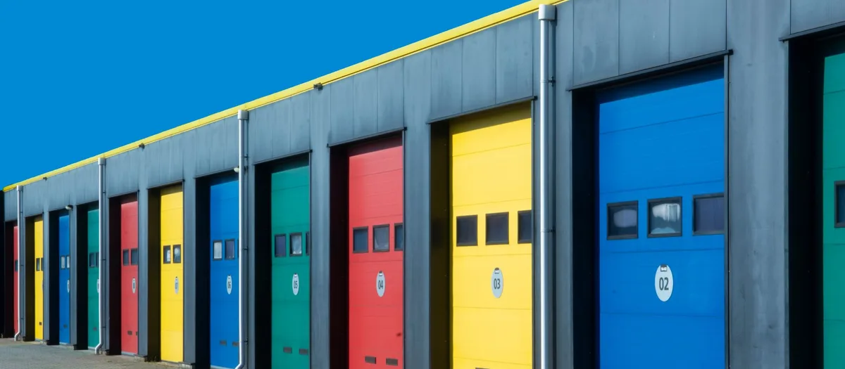 Reihe von Lagerboxen mit farbigen Rolltoren und aufgemalten Nummern unter blauem Himmel