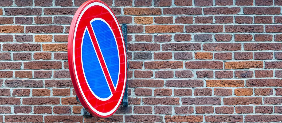 Rundes Verkehrszeichen für eingeschränktes Haltverbot, blaue Fläche mit rotem Rand und rotem Schrägbalken, an einer Backsteinwand