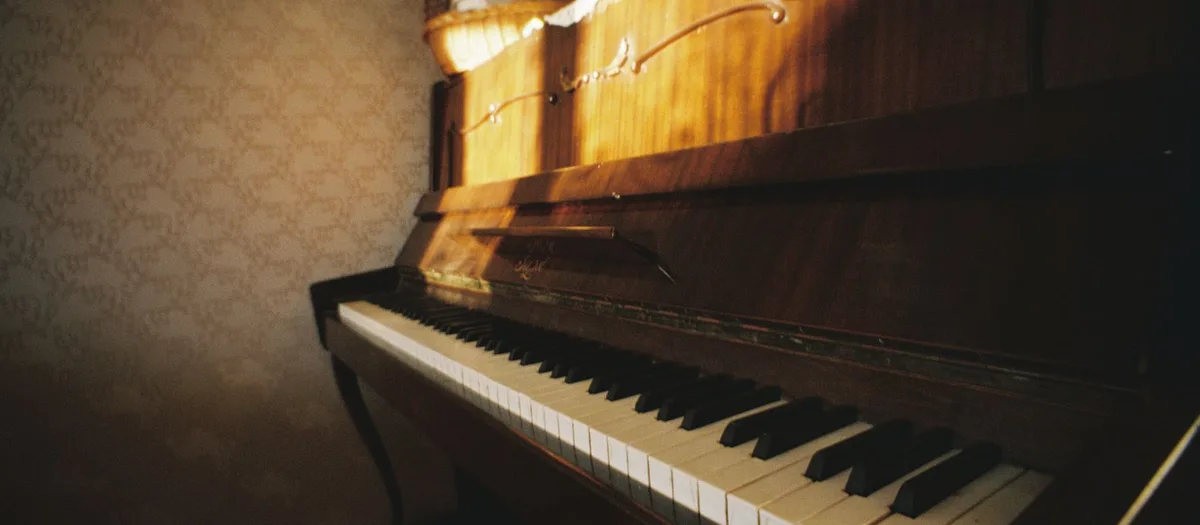 Altes Klavier aus dunklem Holz mit vergilbten Tasten, von der Seite fotografiert, dahinter gemusterte Tapete