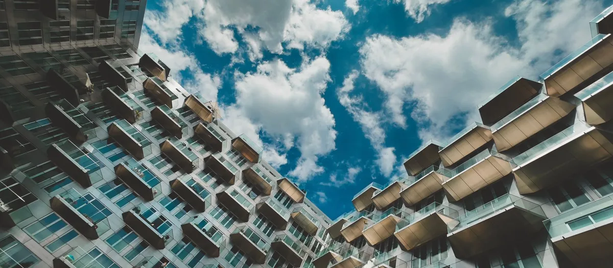 Blick von unten an einer Wohnhausfassade hinauf, Reihe um Reihe vorspringende Balkone vor bewölktem Himmel