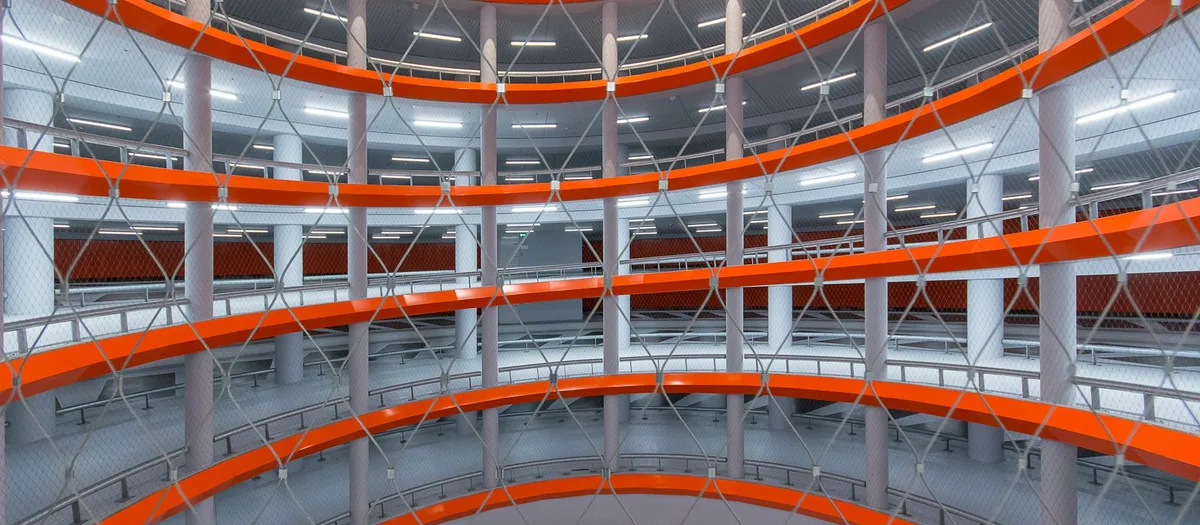 Blick in ein mehrgeschossiges Parkhaus mit umlaufenden Rampen und orange abgesetzten Brüstungen