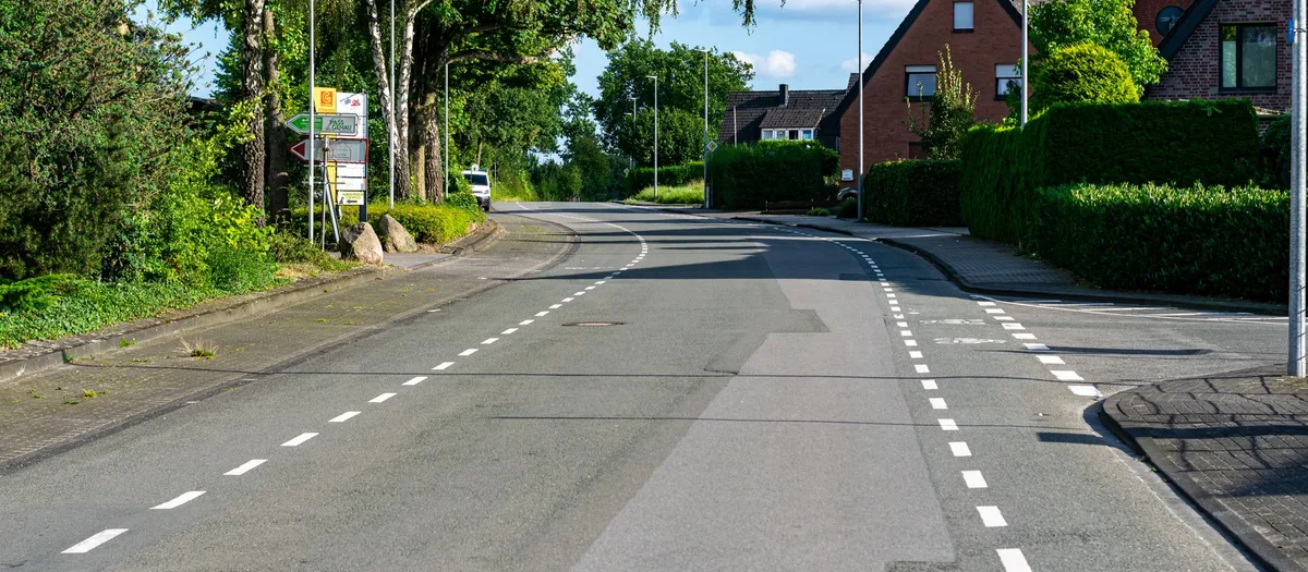 Ruhige Wohnstraße am Ortsrand mit hohen Hecken, Backsteinhäusern und breitem Gehweg