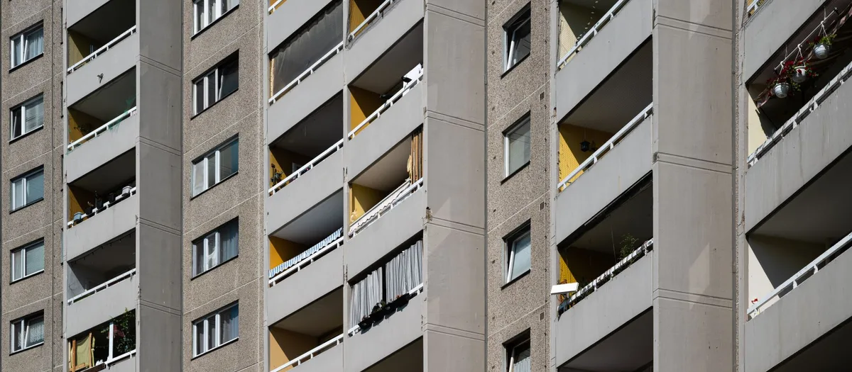 Fassade eines Plattenbaus aus der Nähe: Loggien mit weißen Geländern, Waschbetonplatten und einzelne gelbe Farbfelder