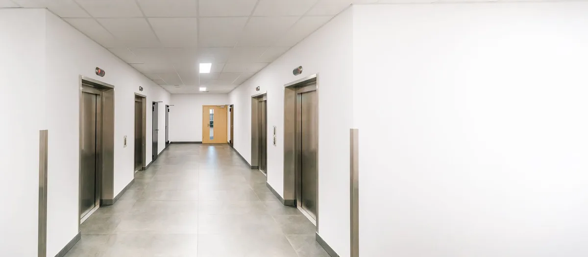 Flur mit vier Aufzugstüren aus gebürstetem Edelstahl, heller Fliesenboden, abgehängte Decke